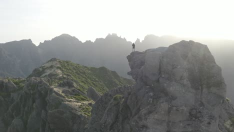 A-man-is-standing-alone-on-the-edge-of-Pico-Grande-mountain-in-Madeira-during-a-sunrise-over-the-beautiful-landscape