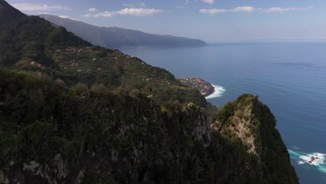 A-drone-clip-flying-backwards-away-from-a-young-man-standing-on-the-edge-of-a-cliff-on-top-of-a-mountain-in-Madeira