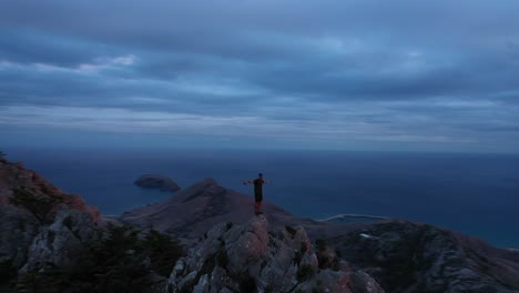 Young-man-stretches-out-arm-on-top-of-mountain-in-Porto-Santo,-Madeira