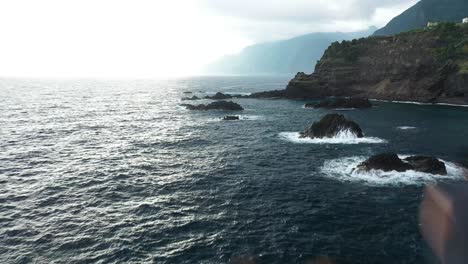 Drone-clip-flying-by-a-young-and-fit-man,-standing-on-the-top-of-a-cliff-next-to-Sexial-Natural-Pools-in-Madeira