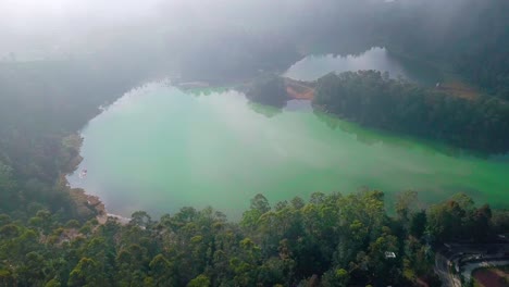 Aerial-birds-eye-shot-of-Lake-Telaga-Warna-in-Indonesia-covered-with-fog-and-clouds-surrounded-by-deep-rainforest-mountains