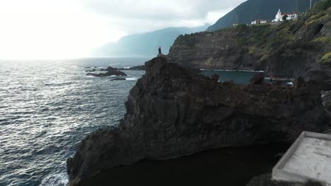 Aerial-clip-flying-by-a-man-standing-on-the-cliff-overlooking-the-ocean-next-to-Seixal-Natural-Pools-in-Madeira