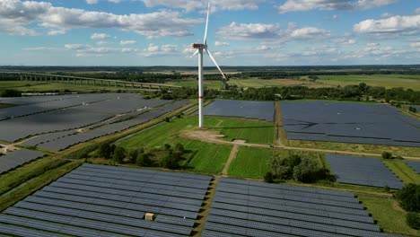 A-windturbine-is-spinning-in-the-middle-of-a-solar-farm-on-a-green-field