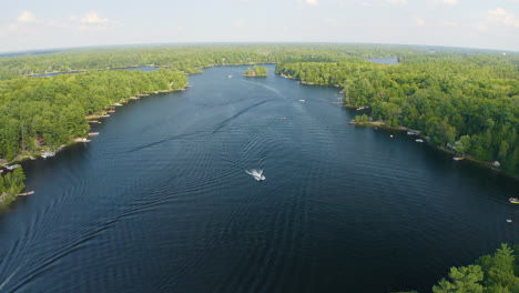 Drone-view-moves-backwards-revealing-multiple-boats-driving-along-the-surface-of-a-beautiful-blue-river-surrounded-by-trees