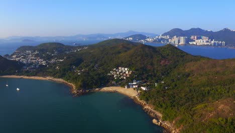 Drone-shot-traveling-forward-above-a-tropical-island-with-some-villages-and-beach-among-the-mountains-and-forest-during-a-sunny-day-2