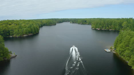 Aerial-view-following-a-boat-with-waterskier-behind-it-driving-down-a-river-on-a-summer-day,-before-the-waterskier-eventually-falls