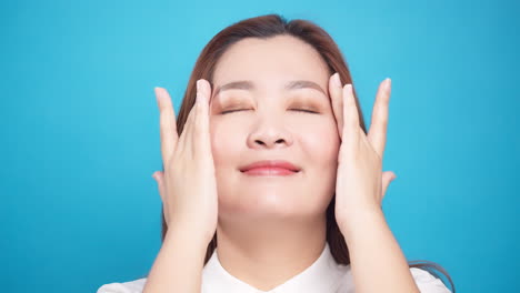 Nahaufnahme-Einer-Perfekten-Hübschen-Asiatischen-Frau,-Die-Das-Gesicht-Sanft-Mit-Anti-Aging-Balsamcreme-Für-Wellness-Hautpflege-Auf-Blauem-Hintergrund-Reibt-3