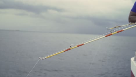 Close-up-of-two-fishing-rods-bent-off-the-side-of-a-boat-in-the-ocean,-moving-up-and-down-in-the-morning,-clouds