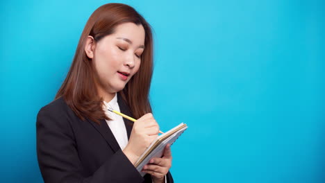 Asiatische-Sekretärin-Geschäftsfrau,-Die-Ein-Notizbuch-Hält-Und-Mit-Listeninspirationsstrategie-Für-Erfolg-Auf-Blauem-Hintergrund-Denkt-1
