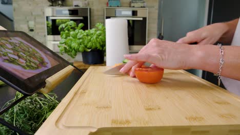 Close-up-of-someone-cutting-a-tomato-while-watching-a-tablet-on-food-preparation-inside-of-a-modern-stylish-home-kitchen