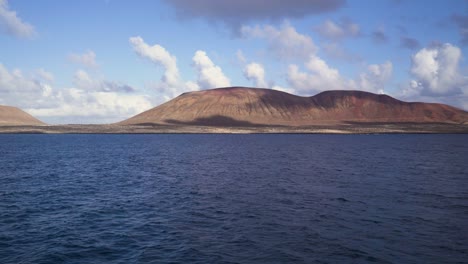 Shot-taken-from-the-sea-looking-towards-the-shore-where-there-are-arid-and-dry-brown-lands-that-form-mountains-taken-during-a-sunny-day-with-clouds