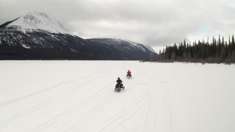 Drone-shot-of-two-people-snowmobiling-on-a-frozen-lake