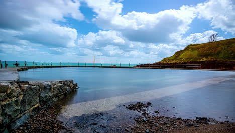 Hyperlapse-Aufnahme-Von-Fliegenden-Wolken-über-Dem-Strandpool-In-Guernsey-Mit-Meerblick-Im-Hintergrund
