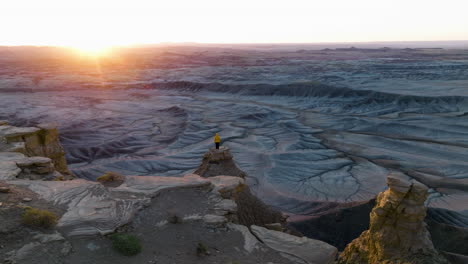 Adventurous-Girl-Wearing-Yellow-Jacket,-Admiring-Beautiful-Sunrise-While-Standing-On-Dangerous-Edge-Of-Abrupt-Canyon-In-Utah,-USA