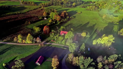 Descending-aerial-shot-of-house-in-rural-area-with-fields-and-colorful-trees-at-sunset