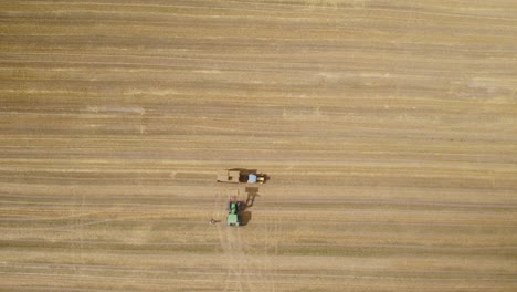Farmers-pile-up-the-load-of-square-hay-bales-in-tractor-trailer,-bird's-eye-view