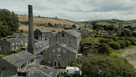 Rooftop-Aerial-footage-of-a-industrial-rural-village-with-old-mill-and-chimney-stack-surrounded-by-fields
