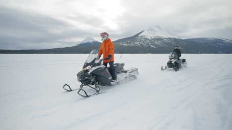 Slow-motion-tracking-shot-of-two-people-snowmobiling-on-a-frozen-lake