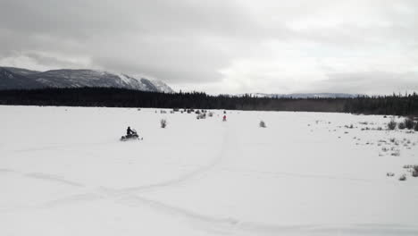 Drone-shot-of-two-people-snowmobiling-on-a-field