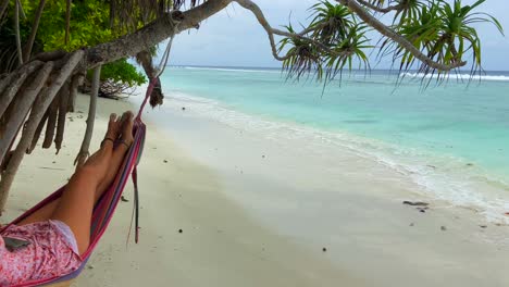 Static-shot-of-young-tanned-girl-rocking-peacefully-in-a-hammock-on-a-palm-tree-on-a-tropical-beach-paradise-in-Maldives