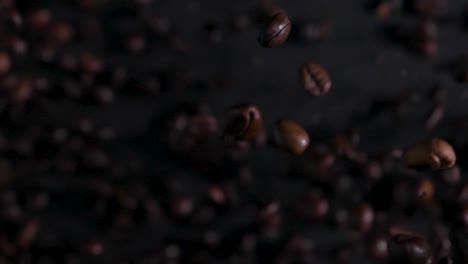 Studio-shot-of-roasted-coffee-beans-bursting-into-the-air,-transition-to-slow-motion-falling-back-then-changing-back-to-real-time-on-the-black-background
