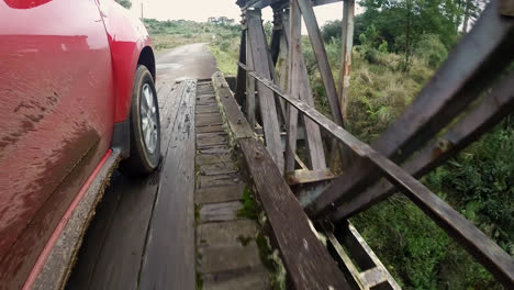Side-view-of-muddy-car-crossing-wooden-bridge-over-river