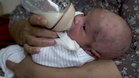 Eine-Nahaufnahme-Eines-Neugeborenen-Babys,-Das-In-Den-Armen-Seiner-Mutter-Liegt-Und-Sich-Von-Einer-Flasche-Muttermilch-Ernährt