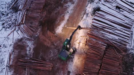 Dramatic-top-down-close-up-aerial-shot-of-timber-manipulator-loading-timber-transportation-18-wheeler-truck-from-nearby-snow-covered-piles-of-cut-mature-pine-trees
