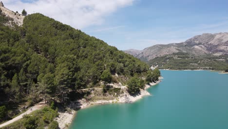 Take-off-over-an-amazing-turquoise-lake-and-mountains-in-Guadalest,-Spain