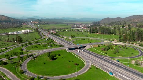 Dolly-in-aerial-view-of-a-traffic-circle-on-route-68-in-Chile,-with-mountains-in-the-background-on-a-sunny-day