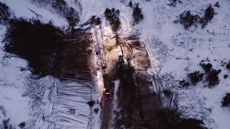 Aerial-drone-stable-observing-from-above-industrial-timber-logging-industry-moving-in-the-winter,-at-dawn-early-morning-before-sunrise