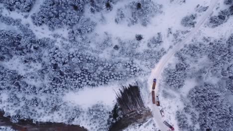 Aerial-drone-shot-18-wheeler-loaded-with-mature-pine-timber-drives-on-dirt-roads-in-snow-covered-winter-logging-camp,-before-sunrise-at-dawn-2