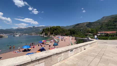 Lovely-sunny-beach-with-large-stone-bridge-situated-in-the-famous-part-of-montenegro-called-Sveti-Stefan-on-a-very-hot-and-sunny-summers-day
