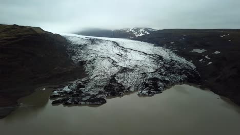 Aerial-landscape-view-over-Sólheimajökull-glacier,-melting-into-water,-in-summer,-Iceland