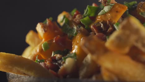 A-stationary-close-up-shot-of-a-full-bowl-of-bacon-and-french-fries-coated-with-cheddar-cheese-and-topped-with-spring-onions