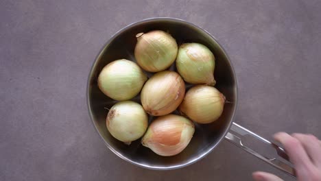 Overhead-View-Of-Hand-Put-Pan-On-The-Table-With-Whole-White-Onions