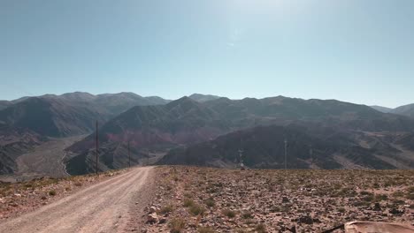 Overtake-Shot-Of-Car-Wreck-Beside-Dirt-Road-With-Mountains-background,-North-Argentina