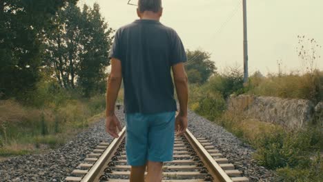 A-man-walks-on-the-tracks-of-an-abandoned-station-in-the-middle-of-nature-in-the-countryside,-reminiscing-about-the-past-when-he-played-there-with-friends