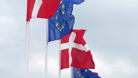 Close-up-gimbal-shot-of-Danish-and-European-Union-Flags-against-cloudy-sky