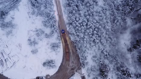 Aerial-drone-shot-18-wheeler-loaded-with-mature-pine-timber-drives-on-dirt-roads-in-snow-covered-winter-logging-camp,-before-sunrise-at-dawn-1