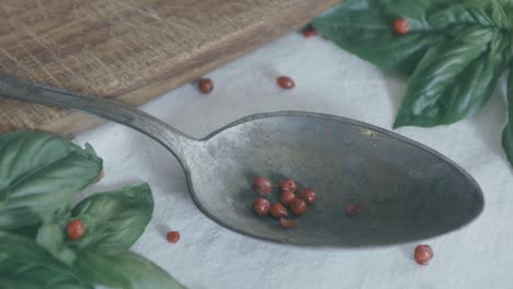 Red-peppercorns-are-dropped-into-a-silver-spoon-and-bounce-all-around-on-the-white-tablecloth