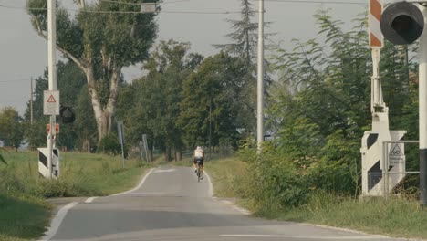 Ein-Fahrradfahrer-Radelt-An-Einem-Sommertag-Eine-Kleine-Landstraße-Hinunter-Und-Weg-Von-Dem-Zimmer-Und-überquert-Einen-Bahnübergang