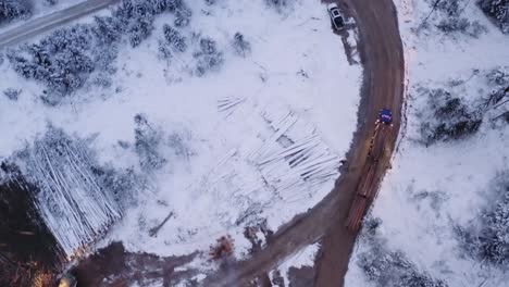 Aerial-drone-shot-18-wheeler-loaded-with-mature-pine-timber-drives-on-dirt-roads-in-snow-covered-winter-logging-camp,-before-sunrise-at-dawn-3