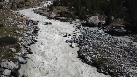 Drone-aerial-view-of-a-muddy-river-with-strong-current,-rocky-valley-in-the-Swiss-alps,-water-from-the-glacier,-global-warming