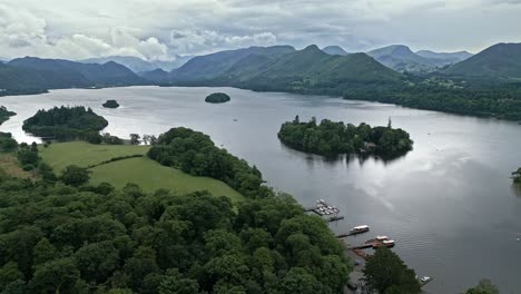 Aerial-footage-of-a-Island-and-house-Derwentwater,-Keswick,-a-calm-lake-with-river-boats-and-a-stormy-sky