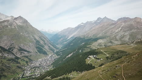 Swiss-alps-landscape:-Rocky-Mountains,-flowery-fields,-fir-forest,-hiking-path-and-Zermatt-village,-drone-aerial-view