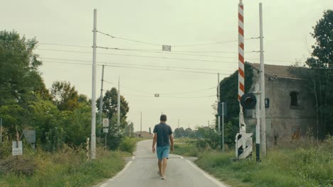 Level-crossing,-a-man-dressed-in-light-blue-and-blue-walks-and-crosses-it,-filmed-from-behind