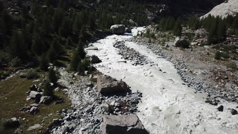 Rocky-valley-in-the-Swiss-alps-with-a-muddy-river-in-the-center,-drone-aerial-view
