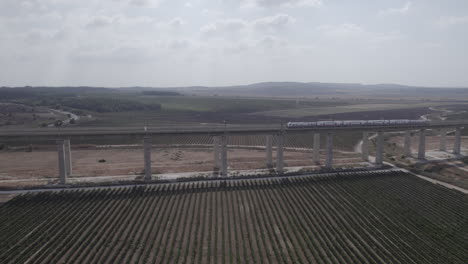 Aerial-Drone-Shot-of-train-passes-on-a-massive-railway-bridge-over-agricultural-fields-and-vineyards---pull-back-reveal