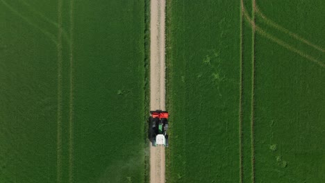 A-tractor-drives-on-a-sandy-path-through-a-green-field---Drone-top-down-shot
